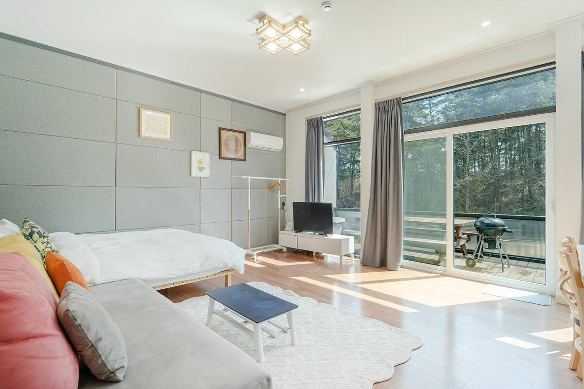 A modern bedroom with a large bed, a TV, and a balcony with a grill.