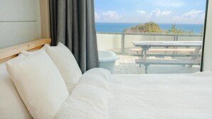 A bedroom with a large bed, a view of the ocean, a balcony with a table and chairs, and a bathtub. - Yangyang In Memory Pension (Yangyang)