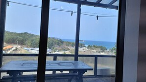 A covered outdoor area with a wooden table and benches, overlooking a coastal landscape with a view of the sea and distant hills. - Yangyang In Memory Pension (Yangyang)