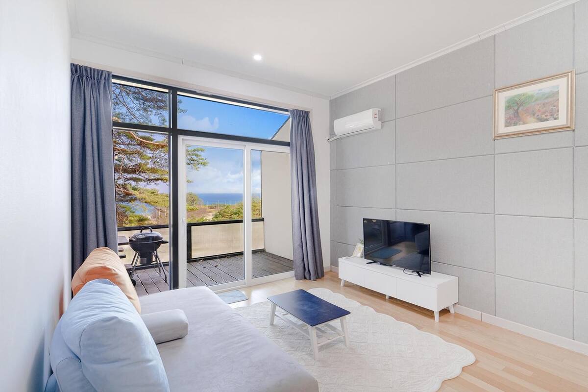 A modern living room with a large TV, a sofa, and a view of the outdoors.