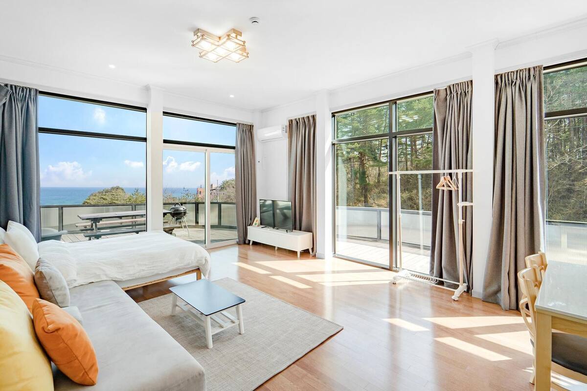 A spacious bedroom with a large bed, a sofa, a small table, and a balcony with a view of the sea.
