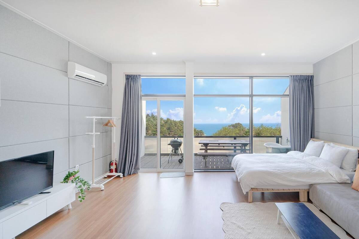 A modern bedroom with a large bed, a TV, and a balcony with a view.