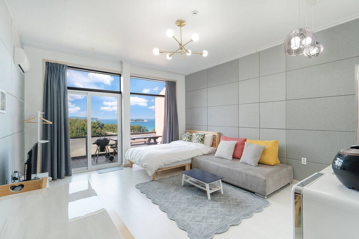 A modern bedroom with a bed, a sofa, a small table, and a large speaker.