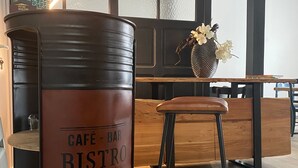A café bar bistro with a large metal barrel labeled 'CAFÉ - BAR BISTRO' and a wooden stool.