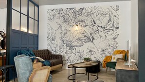 A modern living room with a large floral wall mural, a brown leather sofa, a blue armchair, and a round coffee table.