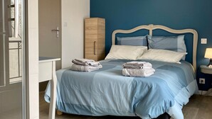 A neatly made bed with a blue bedspread and pillows, a wooden wardrobe, and a bedside table with a lamp.