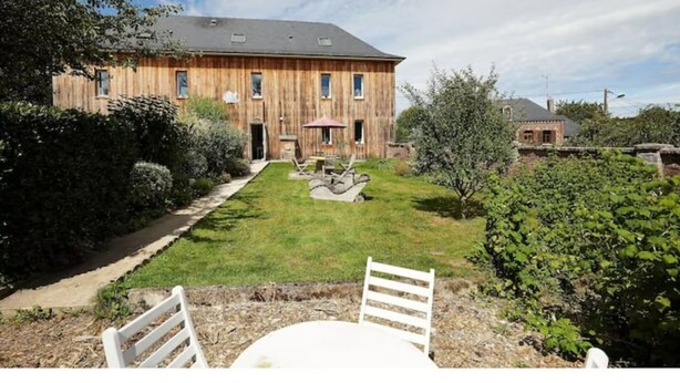 Une maison en bois avec une pelouse bien entretenue et un patio comprenant une table et des chaises.