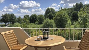 Une table en bois et deux chaises sur un balcon donnant sur des arbres et un ciel nuageux.