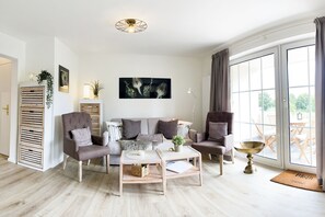 Un salon moderne avec un canapé, des fauteuils, une table basse et une grande fenêtre agrémentée de rideaux.