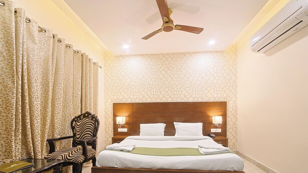 A hotel room with a bed, a chair, a table, a ceiling fan, and an air conditioning unit. - Hotel Green - Behind Parmarth Niketan (Rishikesh)