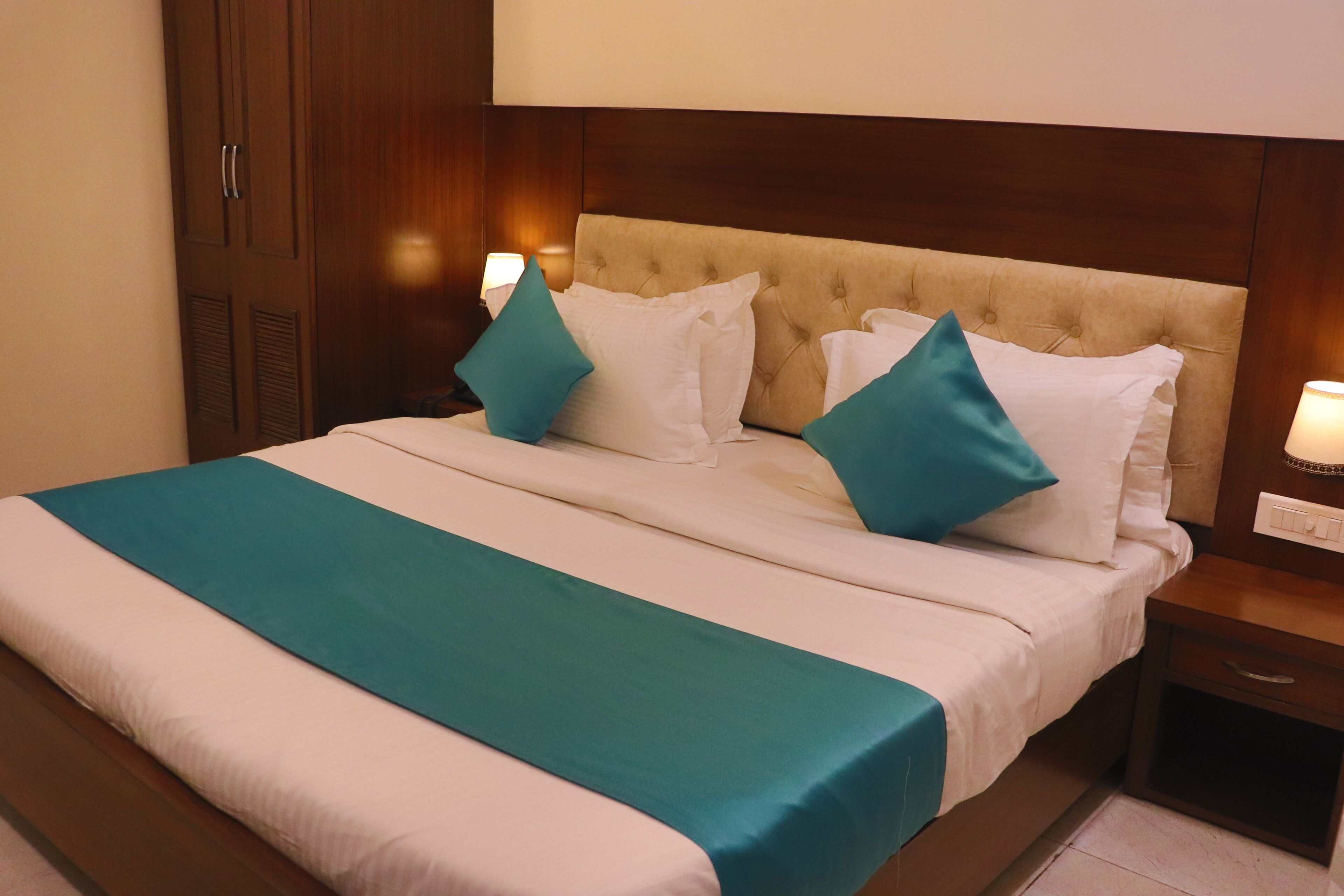 A neatly made bed with a teal and white bedspread, a tufted headboard, and two bedside lamps.