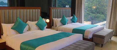 A hotel room with two beds, each with a headboard, a bench, and a nightstand with a lamp.