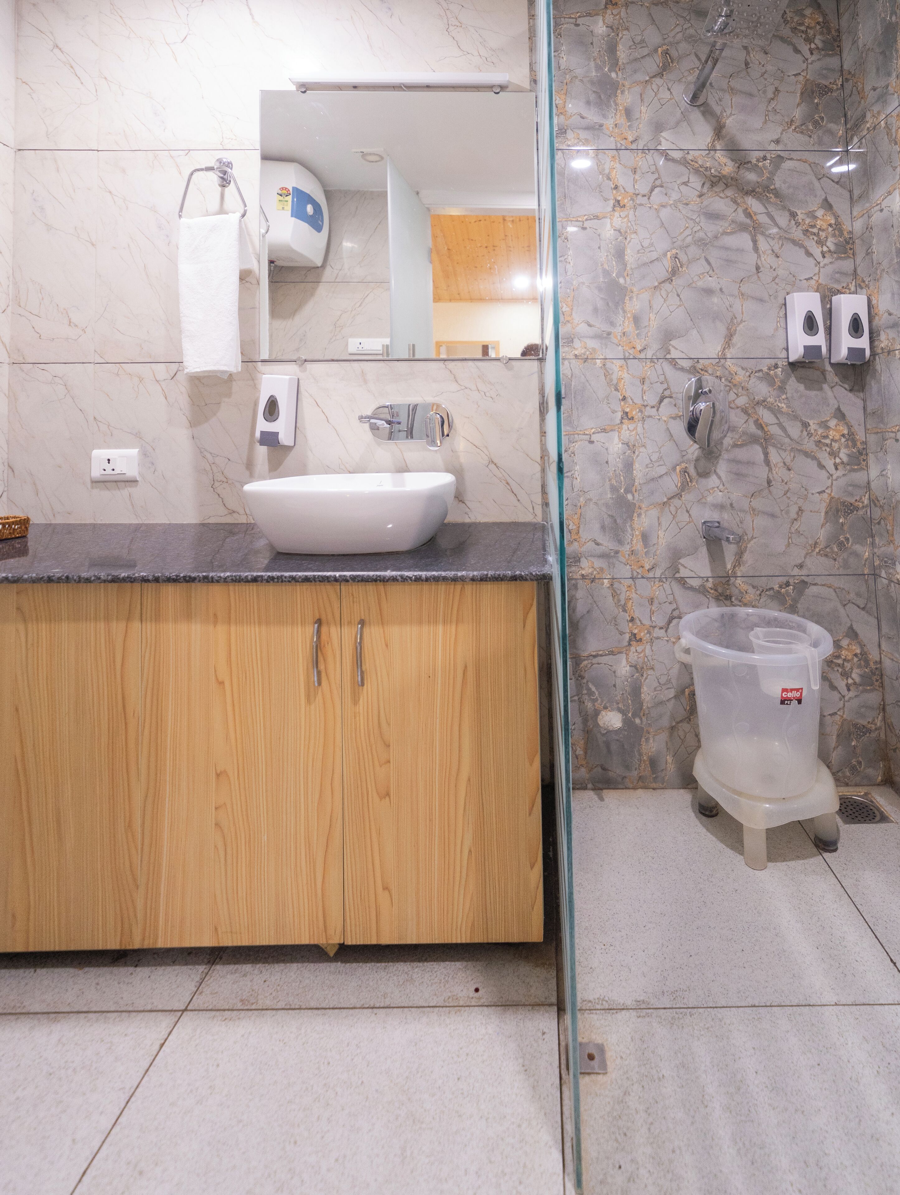 A bathroom with a white sink, wooden cabinets, a glass shower enclosure, and a marble backsplash.