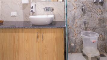 A bathroom with a white sink, wooden cabinets, a glass shower enclosure, and a marble backsplash.