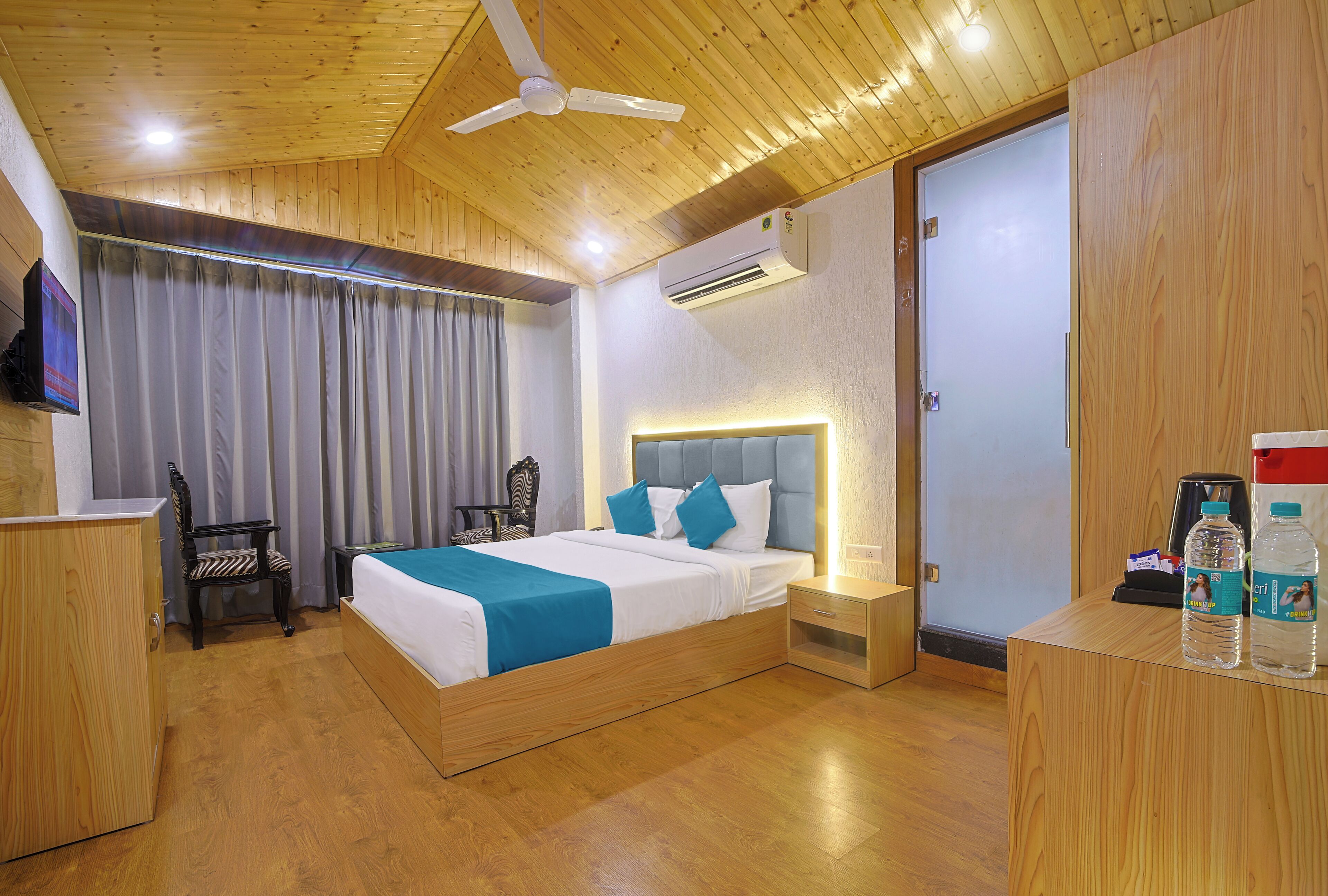A neatly arranged bedroom with a bed, a chair, a desk, and a small table with water bottles.