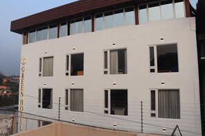 A modern hotel building with a white facade, multiple windows, and a prominent logo on the left side. - Hotel Green - Behind Parmarth Niketan (Rishikesh)