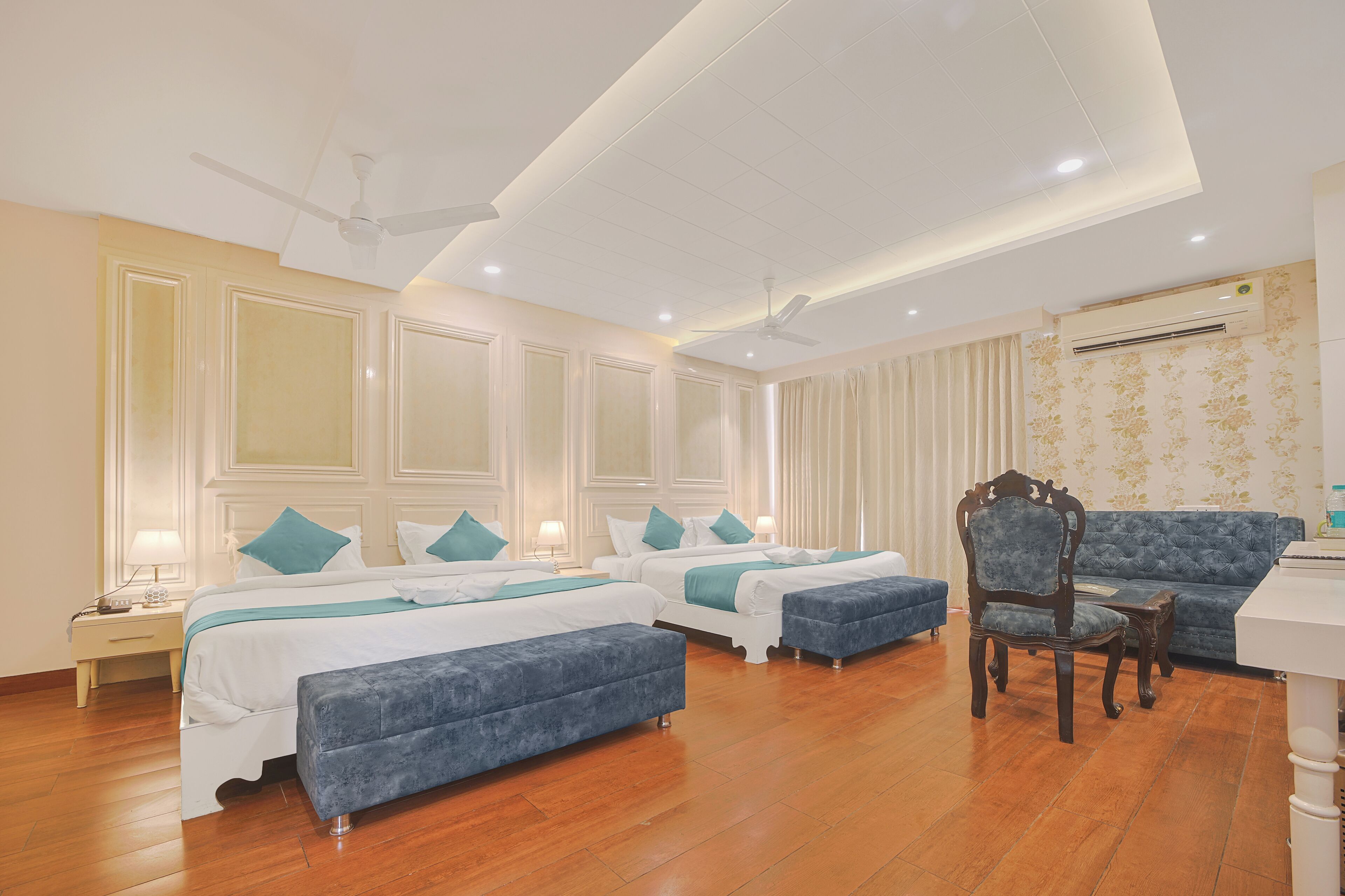 A hotel room with two beds, a sofa, a chair, a desk, and a ceiling fan.