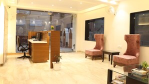 A modern office space with a reception desk, two patterned chairs, a glass table, and a potted plant. - Hotel Green - Behind Parmarth Niketan (Rishikesh)