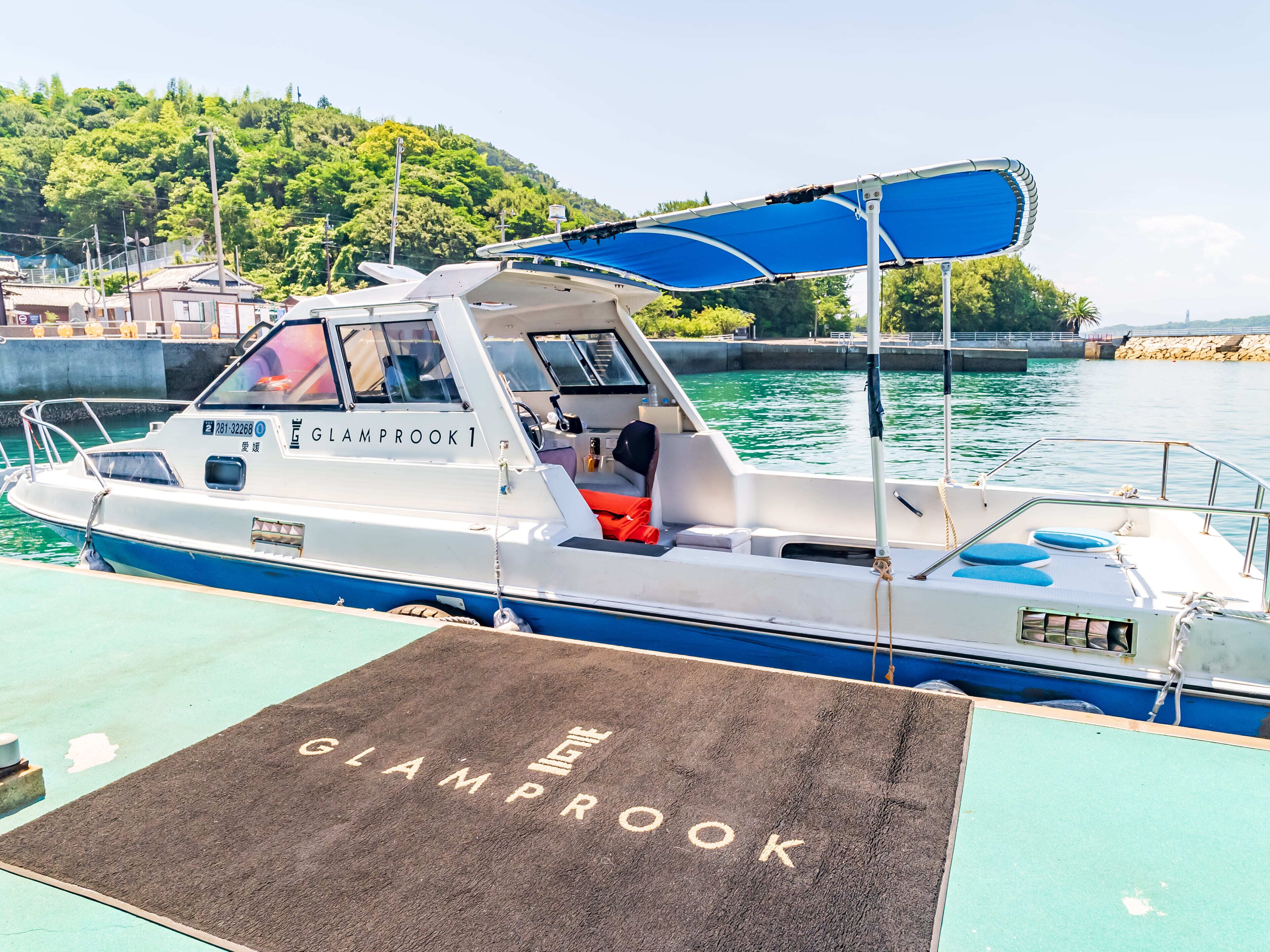 A boat docked at a marina with a name on the side, a covered seating area, and a wakeboard on the deck.