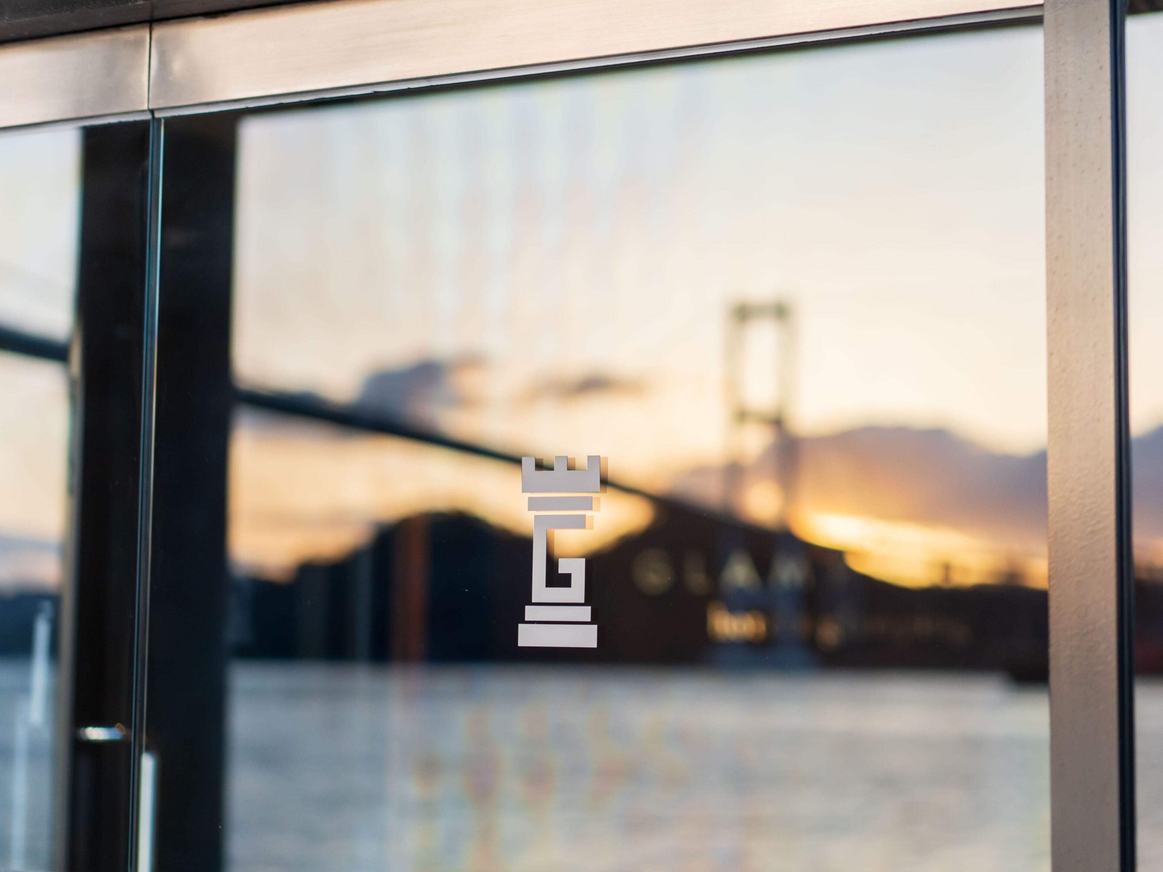 A glass window with a logo and a blurred view of a bridge and sunset.