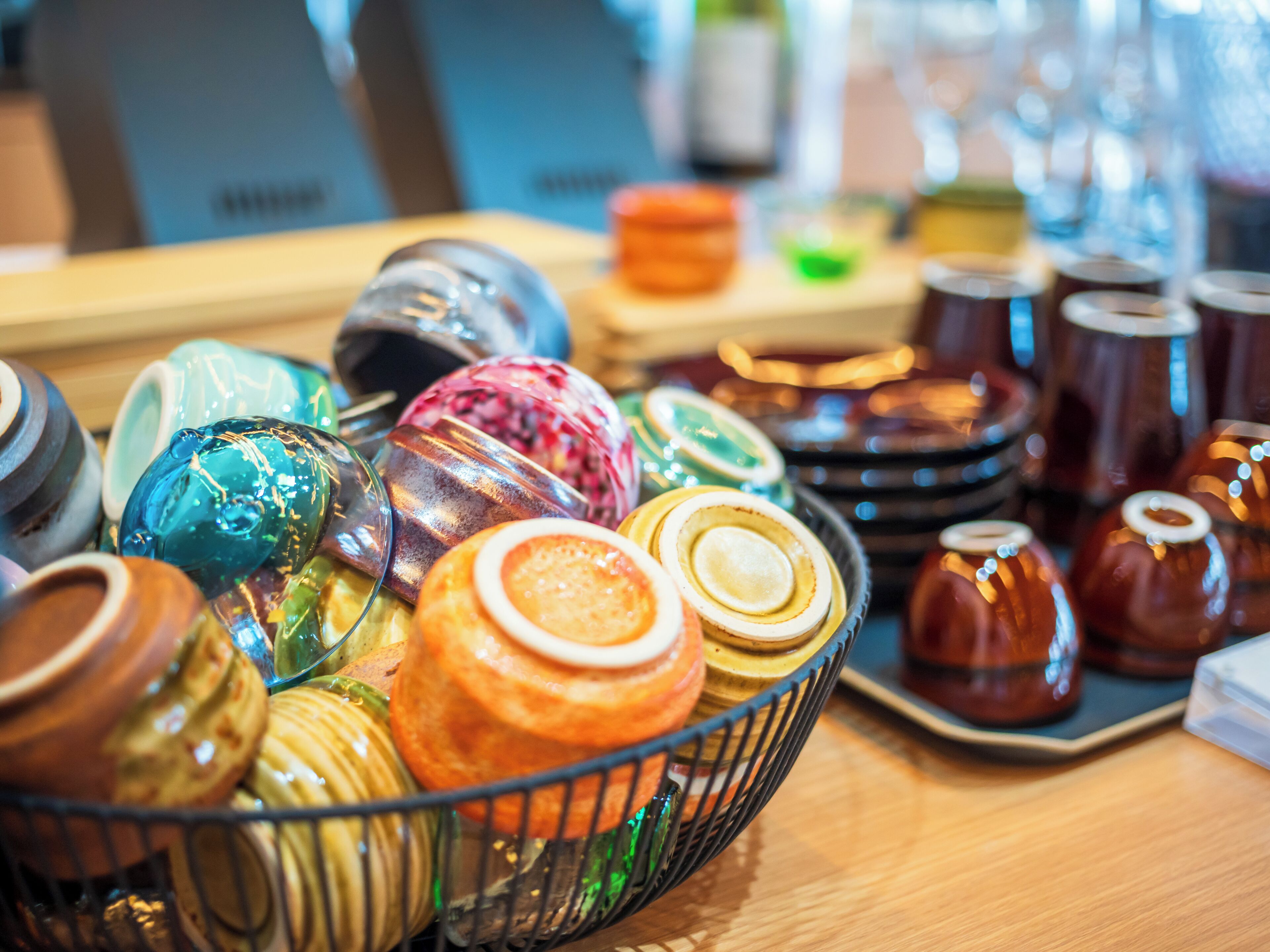 A variety of colorful glassware displayed in a basket on a wooden table.