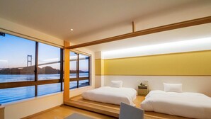 Habitación de hotel con dos camas, vista a un puente, una mesita con planta y juego de té, y una silla.