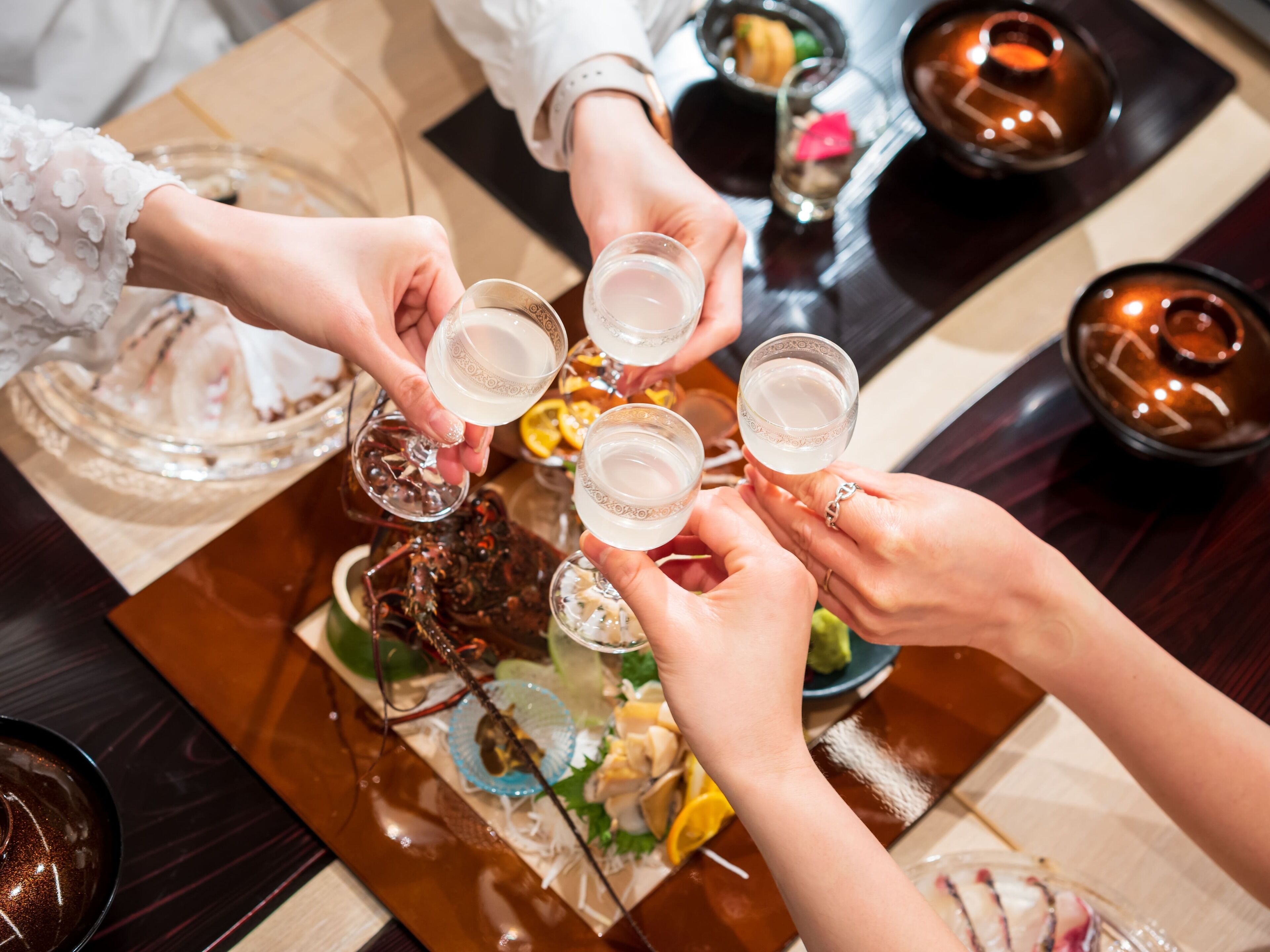 A group of people toasting with glasses at a table with a variety of dishes and drinks.