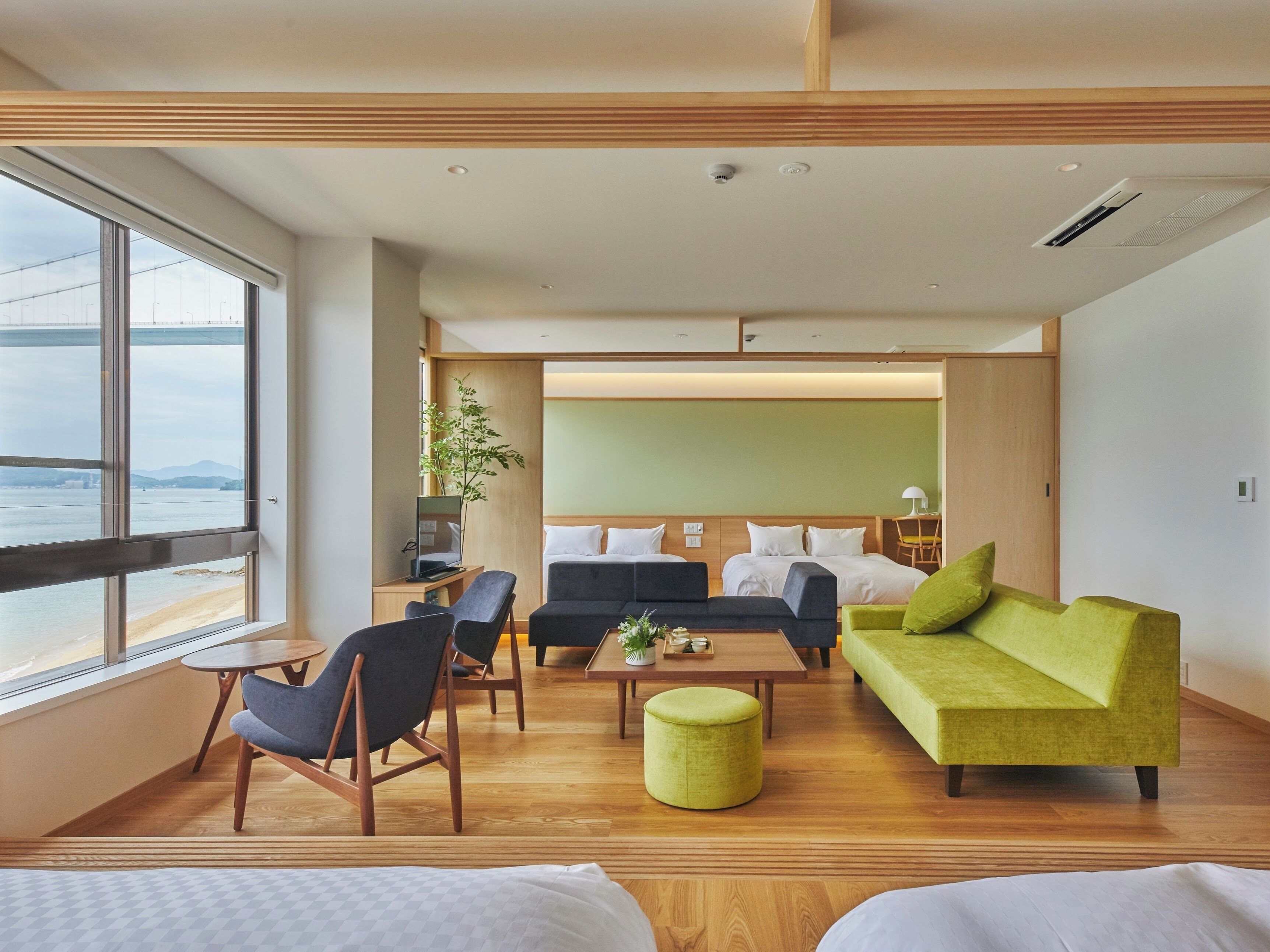 A modern hotel room with a large window, a sofa, a dining table, and a bed.