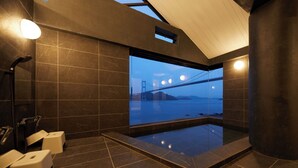Un baño moderno con un ventanal grande, baldosas oscuras y vista a un puente.