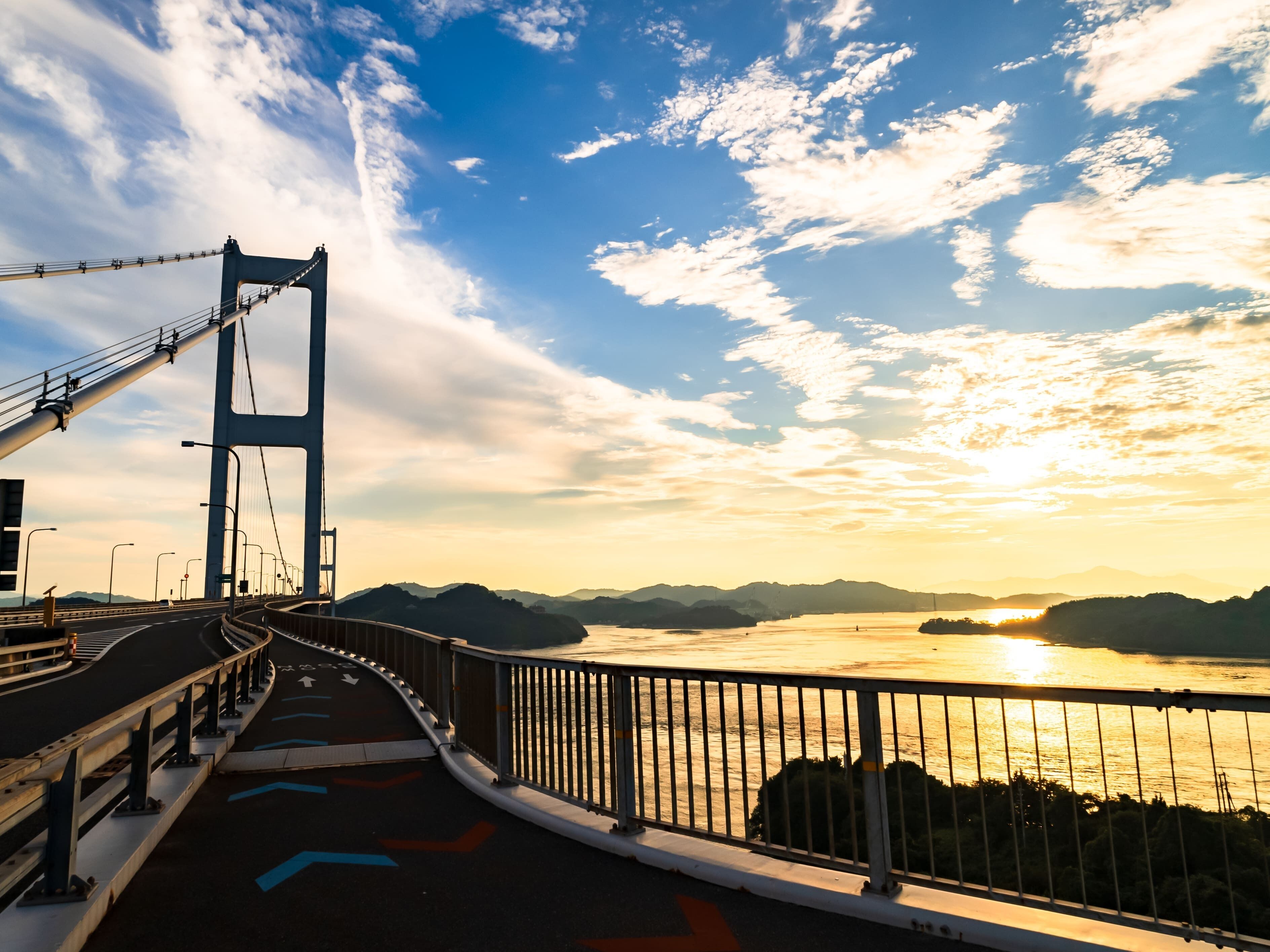 A bridge with a view of a sunset over a body of water and distant mountains.