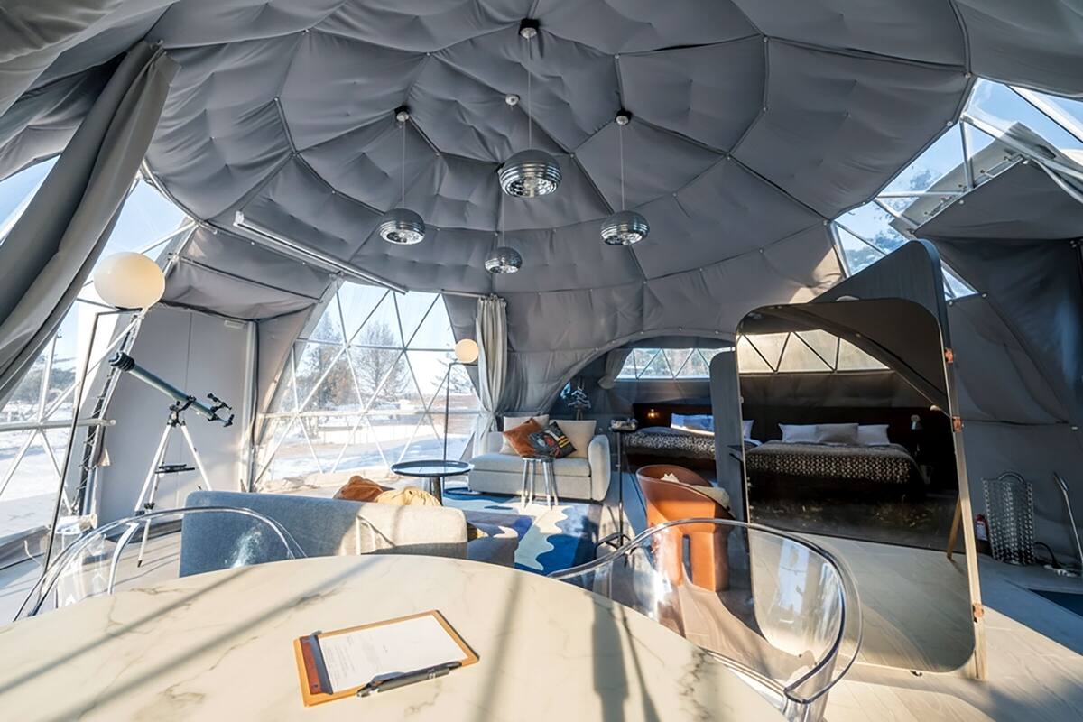 Ein modernes, geräumiges Interieur mit hohen Decken und großen Fenstern, ausgestattet mit einer gemütlichen Sitzecke, einem kleinen Tisch und einer Schlafgelegenheit.