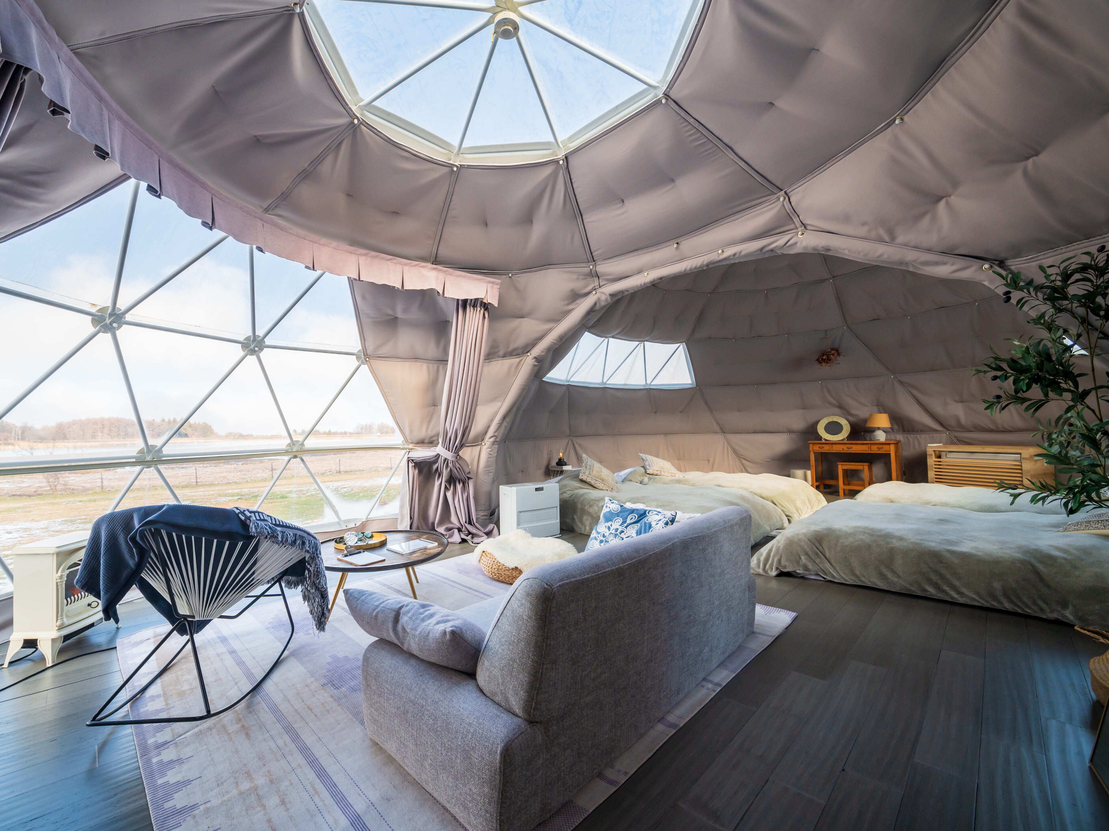 A cozy interior of a geodesic dome with a bed, sofa, and a small table with a lamp.