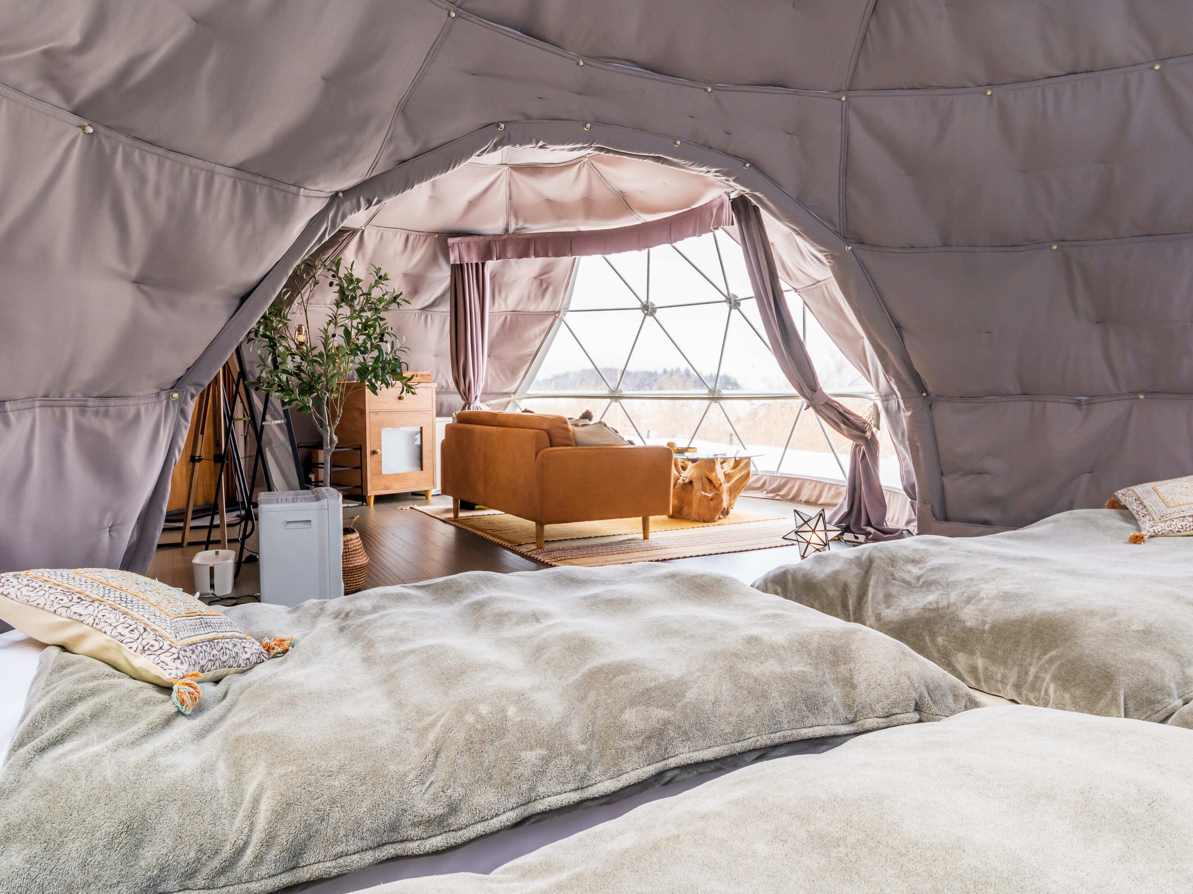 A cozy tented accommodation with a sofa, two beds, a wooden cabinet, and a large window offering a view.