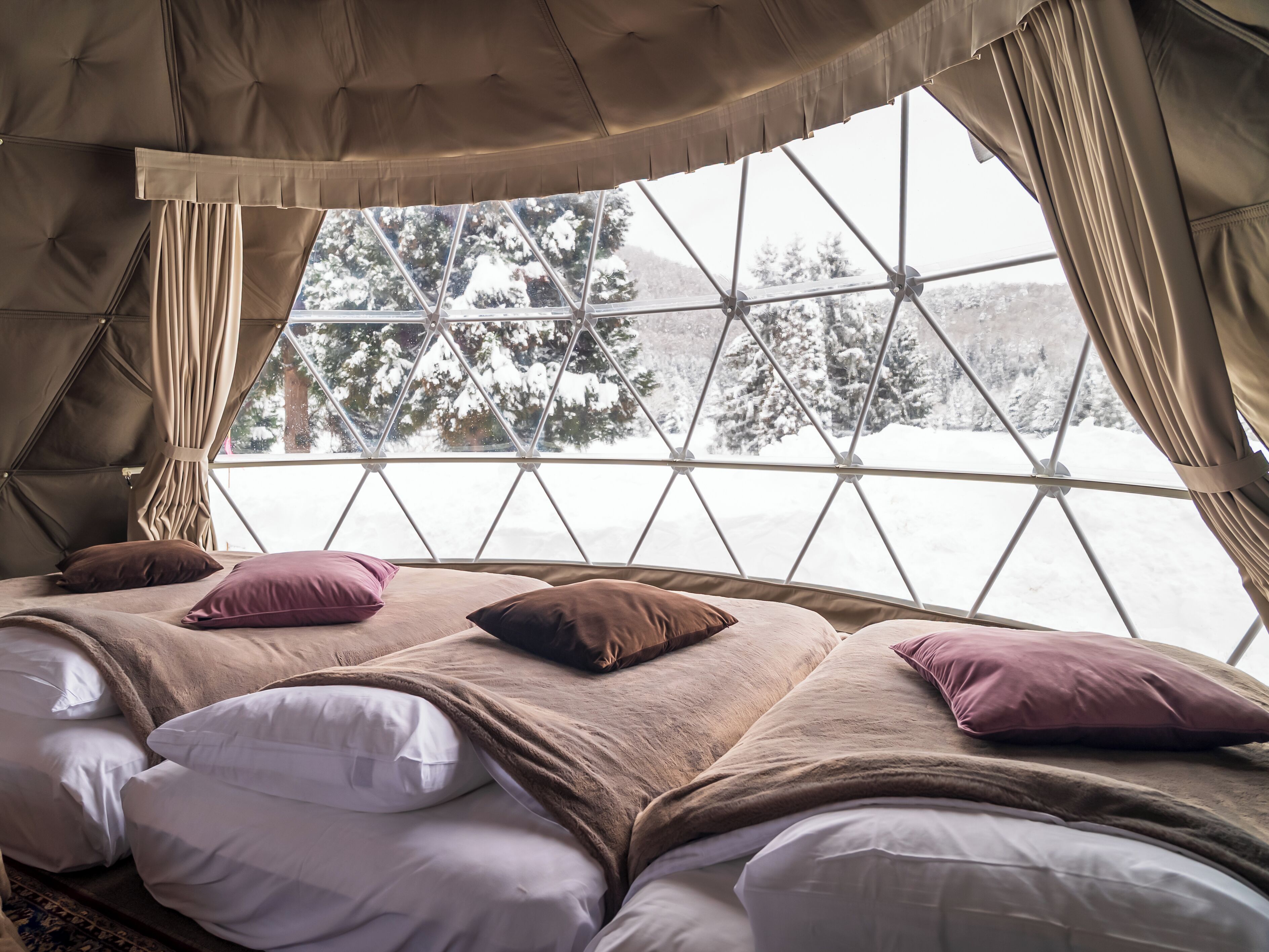 A cozy bed with multiple pillows and a view of a snowy landscape through a large window.