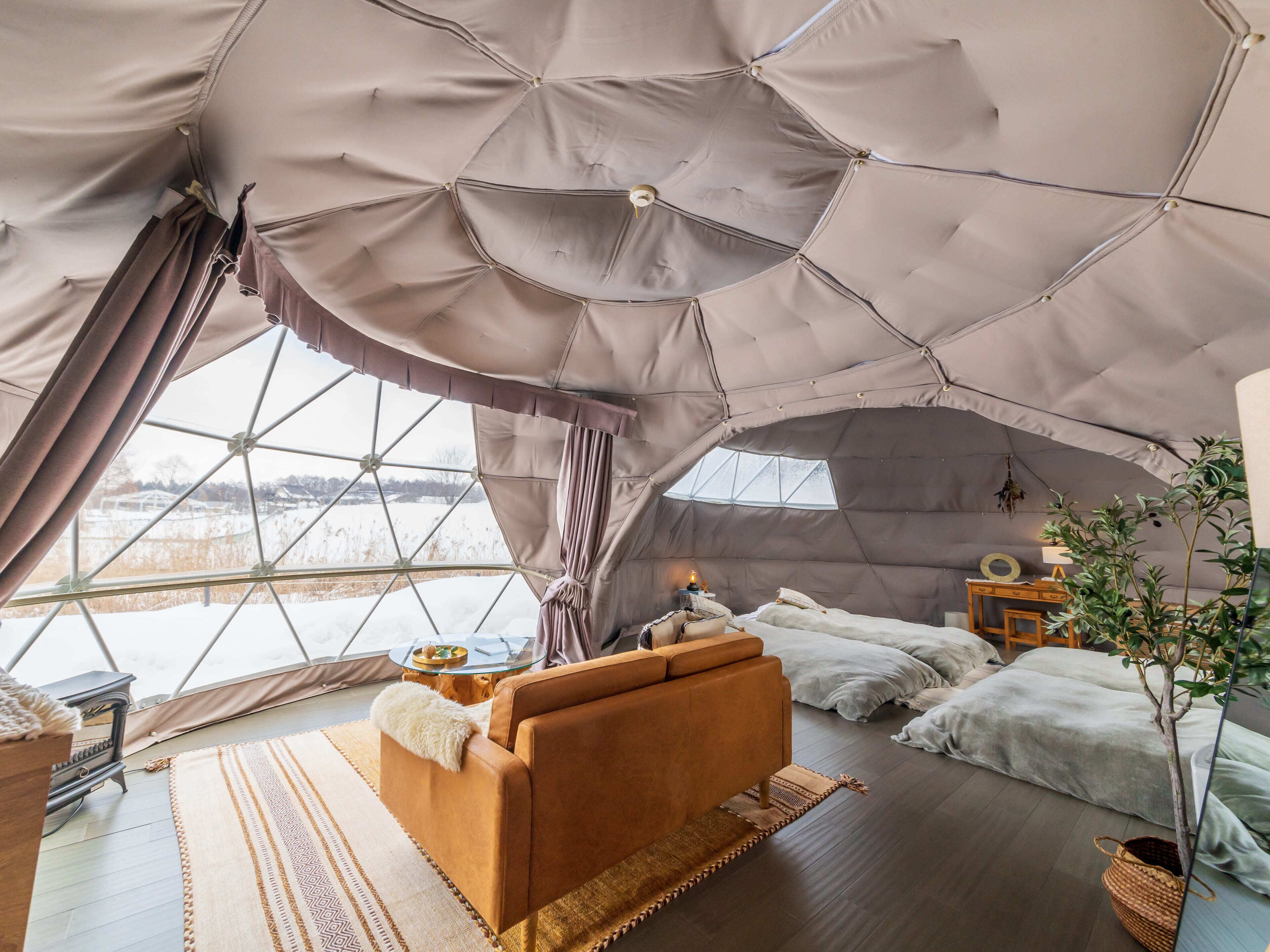 Um interior acolhedor com sofá, cama e uma pequena mesa, tudo sob uma grande estrutura de tenda geométrica.