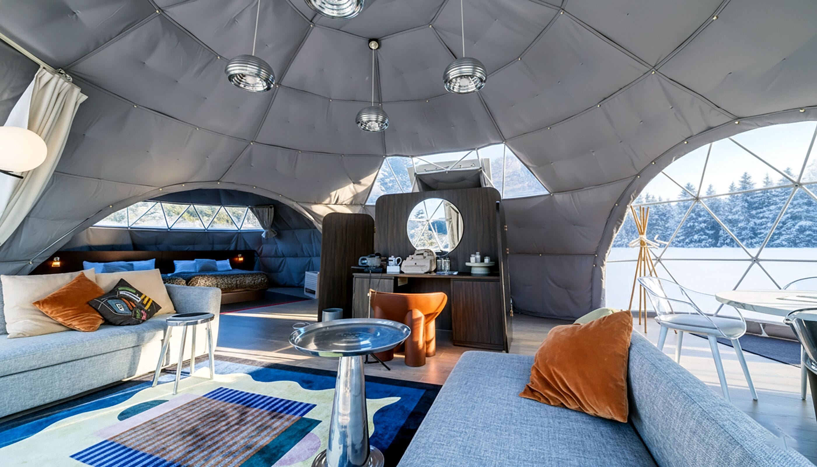 A cozy interior of a dome-shaped tent with a bed, seating area, and a small kitchenette.