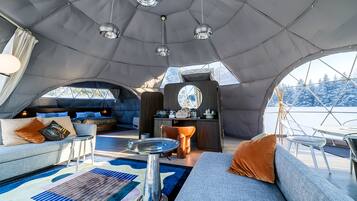 A cozy interior of a dome-shaped tent with a bed, seating area, and a small kitchenette.