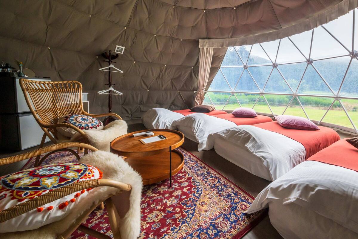 Ein gemütliches Interieur mit einem Bett, einem Sessel, einem kleinen Tisch und Blick durch ein großes Fenster.