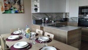 Una cocina moderna con armarios blancos, encimera de mármol y una zona de comedor para cuatro personas, con mesa, sillas y un cuadro de un canal.