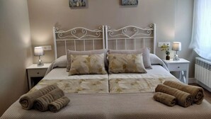 Una cama bien hecha con una colcha estampada, dos almohadas y toallas enrolladas a un lado.
