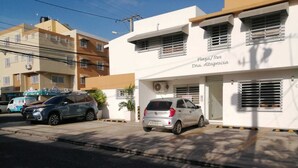 A building with a sign reading "Plaza/Res. Dna. Altagracia" and a parking area with two cars.