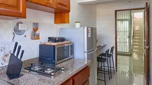 A kitchen with wooden cabinets, a granite countertop, a microwave, a stove, and a refrigerator.