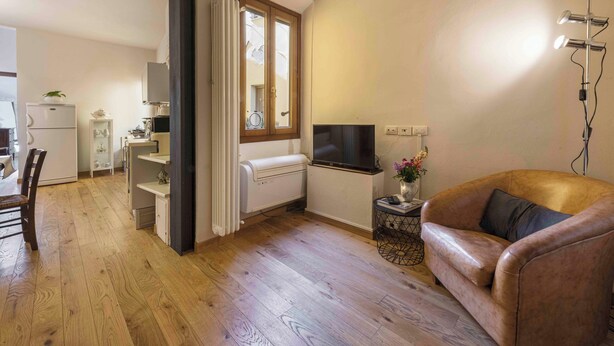A living room with a brown leather sofa, a TV on a stand, and a wooden floor. - Casa Carolina by Mmega (Florence)