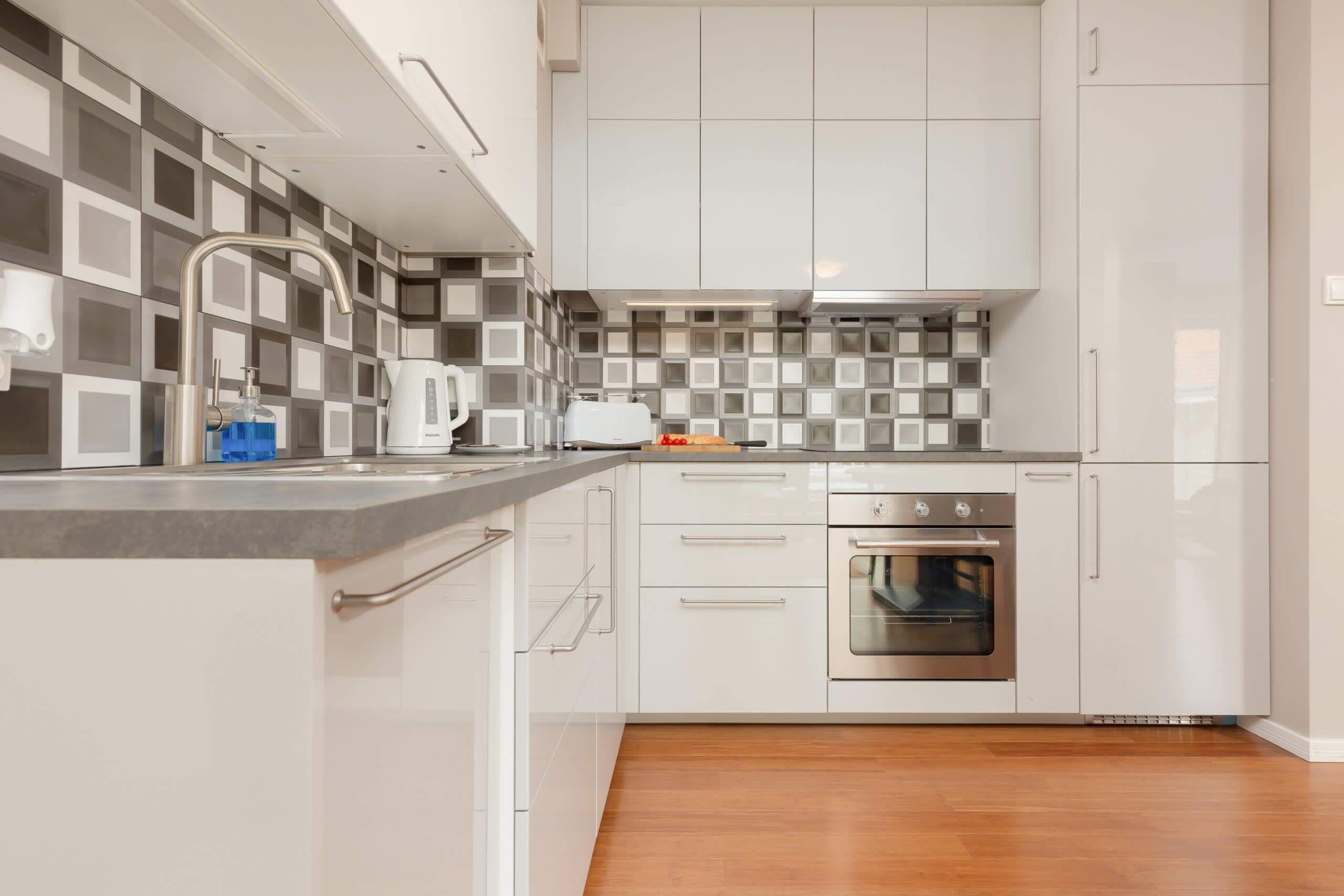 Eine moderne Küche mit weißen Schränken, einem Edelstahlbackofen und einer karierten Spritzschutzwand.