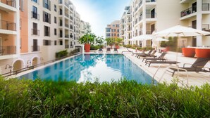 Ein Pool mit Liegestühlen und Sonnenschirmen, umgeben von mehrstöckigen Gebäuden mit Balkonen.