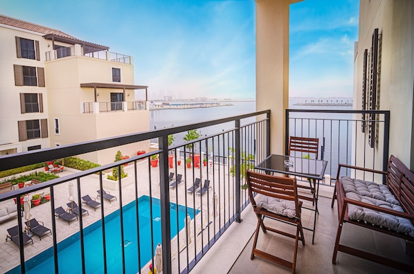 A balcony with a pool, lounge chairs, and a table.