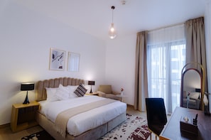 A hotel room with a large bed, two bedside tables, a desk, a chair, a mirror, and a window with curtains.