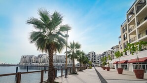 Eine Uferpromenade mit Palmen, einem Zaun und modernen Gebäuden.