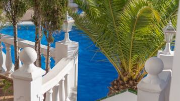 A white balustrade with a view of a blue body of water and a palm tree.