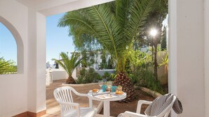 A patio with white chairs and a table, surrounded by plants and a palm tree. - Holiday Park Santa Ponsa (Calvia)